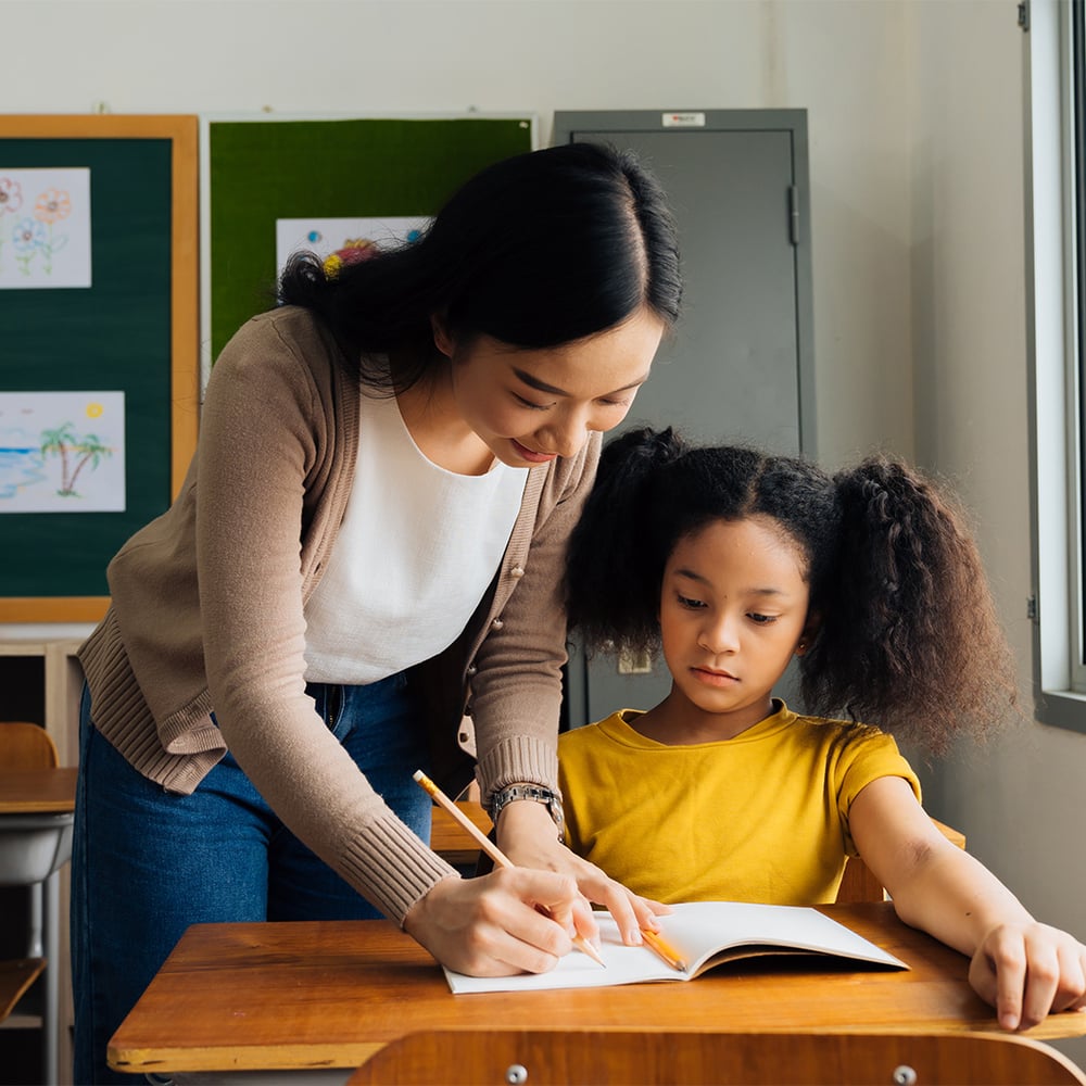 teacher-writing-in-notebook-at-student-desk